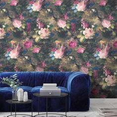 a blue couch sitting next to a table with a vase on top of it in front of a floral wallpaper