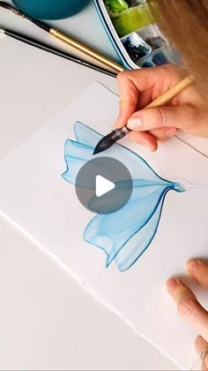 a person is drawing with watercolors on paper and using a brush to draw the flower