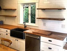 a kitchen with wooden counter tops and white cupboards next to a sink, dishwasher and window