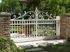 an iron gate with stone pillars and brick pillars in front of a white picket fence