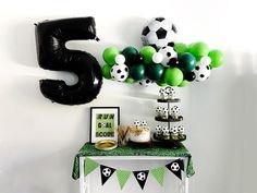 a table topped with lots of balloons and soccer themed items next to a number 5 sign