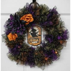 a wreath with purple and orange flowers hanging on the front door, decorated with an image of a witch