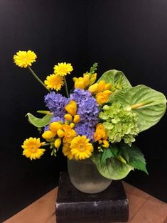 a vase filled with yellow and purple flowers on top of a wooden table next to a black wall