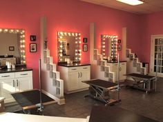 a salon with pink walls and lights on the mirrors, tables and benches in front of them