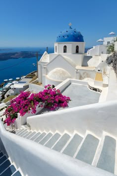 white buildings with blue domes and pink flowers on the steps leading up to them in front of water