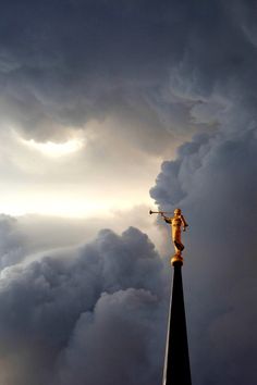 a statue on top of a tall tower under a cloudy sky with sun shining through the clouds