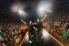 two people on stage in front of an audience with their arms up and hands raised