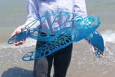 a woman is holding a blue sculpture in front of the water on the beach with her hands