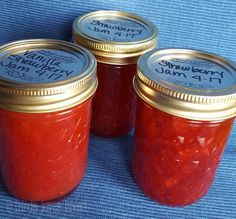 three jars of strawberry jam sitting on top of a blue cloth