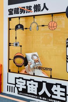 a woman sitting in front of a poster with headphones on her face, reading a book