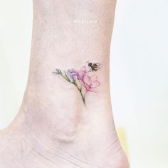 a small tattoo on the ankle of a woman's foot with flowers and a bee