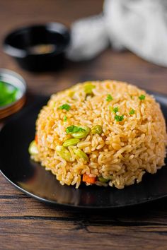 a black plate topped with rice and veggies on top of a wooden table