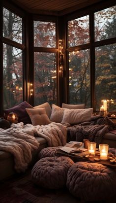 a living room filled with lots of pillows and blankets on top of a couch next to large windows