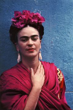 a woman in a red dress with flowers on her head standing against a blue wall