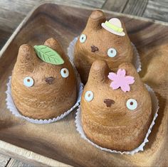 three cupcakes shaped like cats on a wooden tray