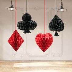 three red and black paper hearts hanging from strings in front of a white wall with chandelier