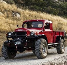 an old red pickup truck driving down a dirt road