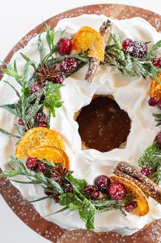 a cake decorated with oranges, cranberries and cinnamon on a wooden platter