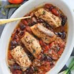 a white bowl filled with chicken and beans on top of a table next to tomatoes