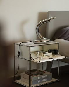 a table with a lamp on top of it next to a book and a bed