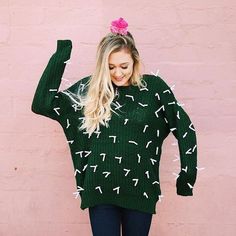 a woman wearing a green sweater with white arrows on it and pink wall in the background