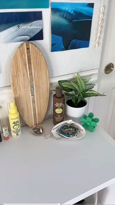 a white table topped with lots of items next to a potted plant and pictures on the wall