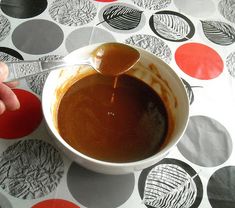 a person is pouring caramel sauce into a white bowl on a patterned tablecloth