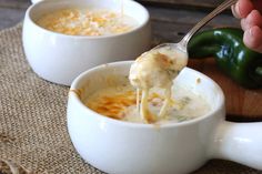 a spoon full of soup with cheese being lifted from it's bowl and another bowl in the background