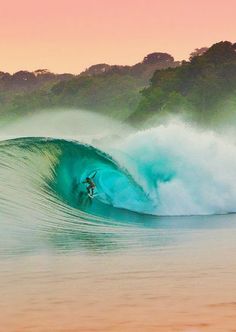 a man riding a wave on top of a surfboard in the ocean at sunset