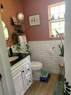 a white toilet sitting in a bathroom next to a sink under a window with potted plants on it