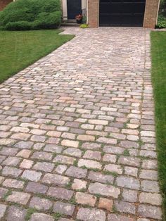 a brick driveway in front of a house with a black garage door and green grass