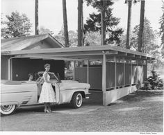 a woman standing next to a car in front of a house with a shed on the roof