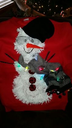 a red shirt with a white snowman on it and lights around the neckline