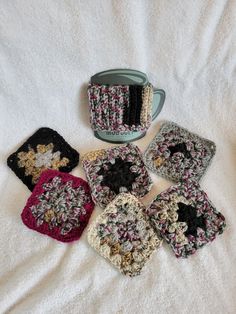 four crocheted coasters and a coffee cup on a white bed with a blanket