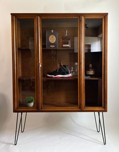 a wooden cabinet with glass doors and black hair pins on the legs, in front of a white wall