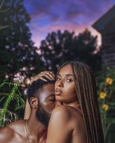 a man and woman are embracing in front of some flowers at night with the sun setting behind them