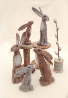 four stuffed rabbits sitting on top of a wooden stand next to a thread spool