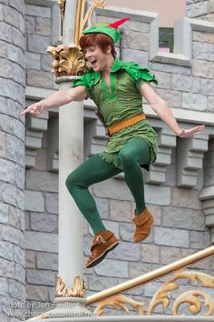 a man dressed as peter pan in front of a castle with his arms out and legs spread wide