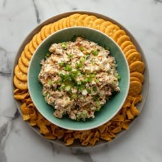 a bowl filled with chicken salad surrounded by crackers on a marble counter top,