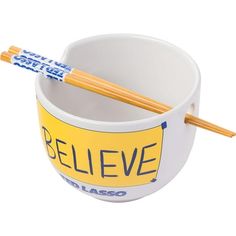 two chopsticks sticking out of a bowl with the word believe on it and yellow lettering