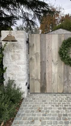 a wooden gate with a wreath on it next to a brick walkway in front of a stone wall