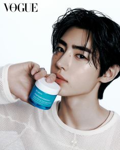 a young man with black hair is holding a jar of cream in his hand and looking at the camera