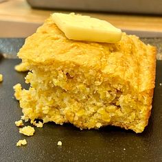 a piece of cornbread with butter on top is sitting on a black cutting board