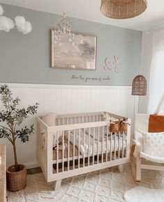 a baby's room with a crib, rocking chair and potted tree