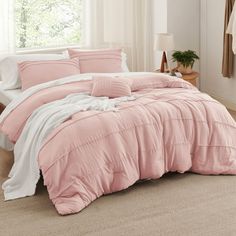 a bed with pink comforter and pillows in a room next to a window on the floor