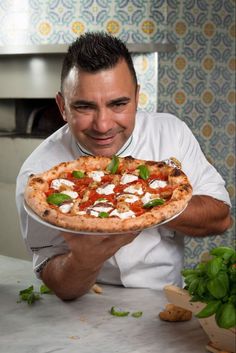 a man holding up a pizza with toppings on it