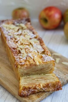 a pastry sitting on top of a wooden cutting board next to some apples in the background