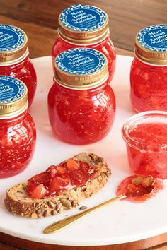 several jars of jelly sit on a plate with bread and jam in the foreground