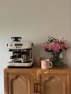 a coffee maker sitting on top of a wooden cabinet next to a vase with flowers