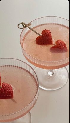 two martinis with strawberries in them on a white counter top and one has a heart shaped stick sticking out of it